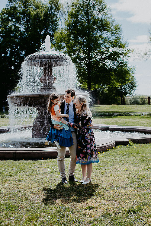 Standesamt - Paar steht innig umschlungen und lachend vor dem Brunnen mit der Tocheter auf dem Arm